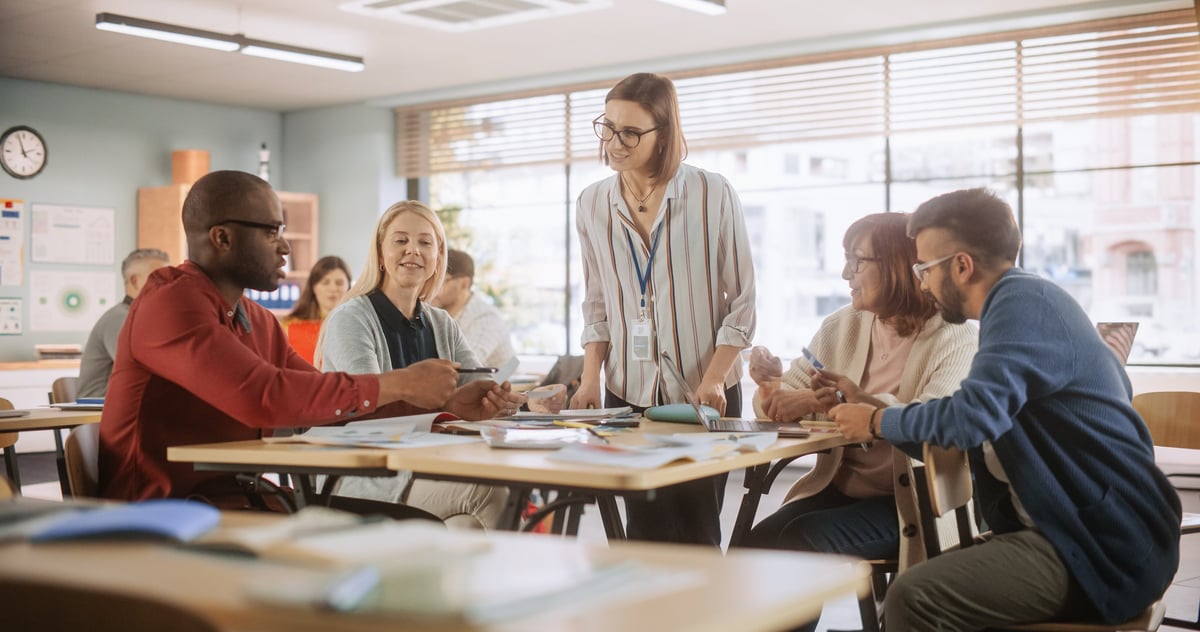 Adult Education Center: Adult Students Learning in Classroom, Working as Two Teams on a Verbal Education Game. Positive Female Teacher Giving Advice