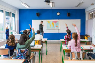 Elementary school students raising hands to answer teacher question