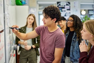 Male student explaining concept to classmates at school, teamwork education