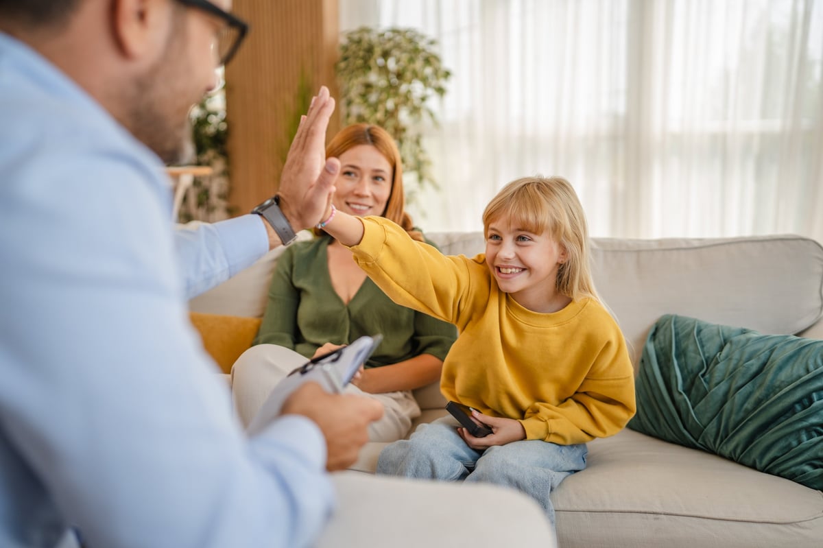 Happy girl giving high five to psychologist during therapy session