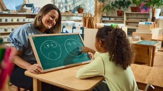 Smiling teacher and child with happy face drawing in classroom therapy activity