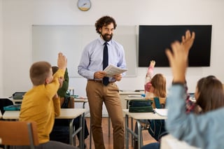 Happy teacher with elementary students raising hands to answer question in classroom